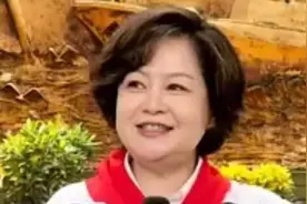 央视主持人鞠萍穿白色上衣，头戴红领巾，与学生大玩自拍图片