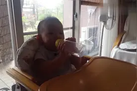 小宝宝坐在餐椅上，拿着装水的奶瓶，对着妈妈笑的样子好可爱