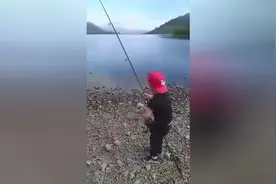 小朋友用腿夹着鱼竿钓上一条鱼，父亲在一旁一边录像一边指挥图片