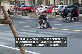 太危险！老人坐轮椅在马路中间倒着走，用脚蹬地还不是往回看图片