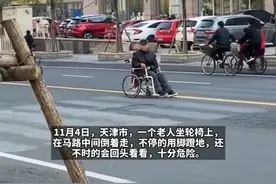 太危险！老人坐轮椅在马路中间倒着走，用脚蹬地还不是往回看图片