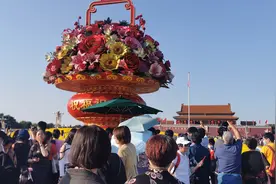 举家出游争相合影，游人在广场大花篮前拍全家福图片