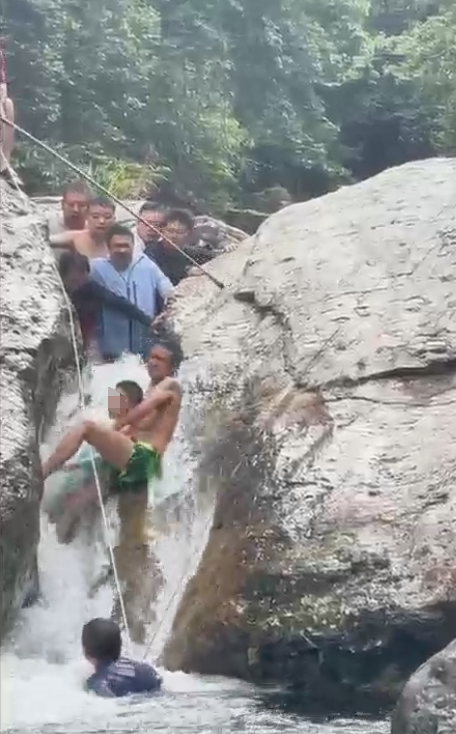 小男孩嬉水被卡两块巨石间，激流中反复挣扎难脱身，好心男子多次施救终成功