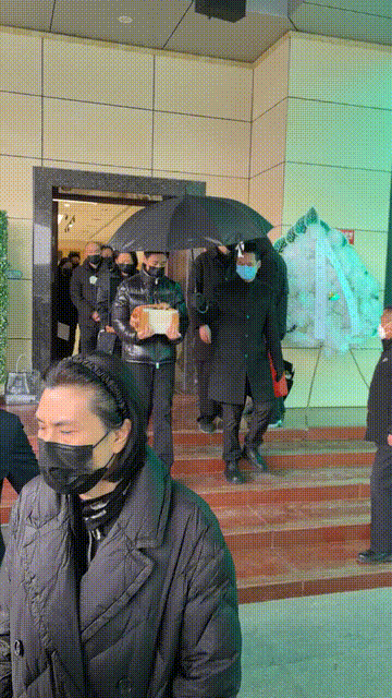 许何弯着腰抱着何晴遗像，背影很难过，许亚军没来给何晴撑伞！