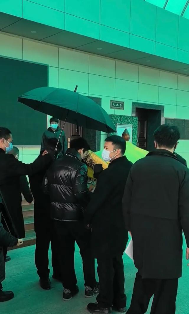 许何弯着腰抱着何晴遗像，背影很难过，许亚军没来给何晴撑伞！