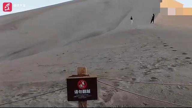 月牙泉景区游客无视喊话翻围栏拍照 围栏上就是警示牌