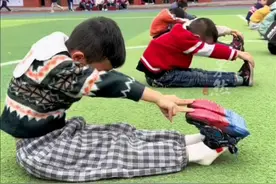 体育课学生练习坐位体前屈，老师让学生努力摸到鞋。学生：你就说摸没摸到吧。图片